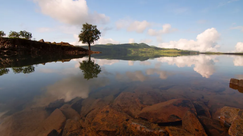 A wide-angle shot of Vaitarna Dam, showing the vast expanse of the reservoir and surrounding hills