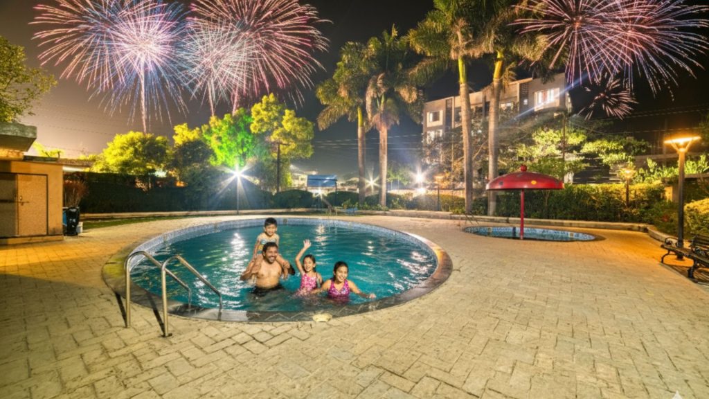 A family laughing and playing in the sparkling blue swimming pool at Hotel Ashwin, Igatpuri add some fireworks