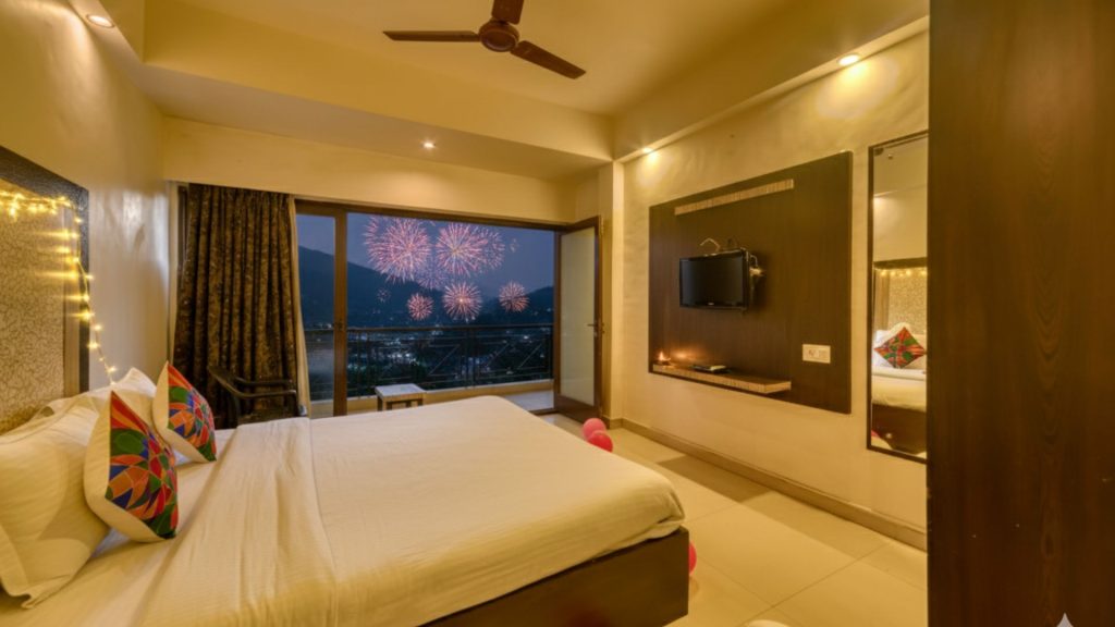 An elegantly decorated Super Deluxe room at Hotel Ashwin, with the balcony door open to a view of the mountains